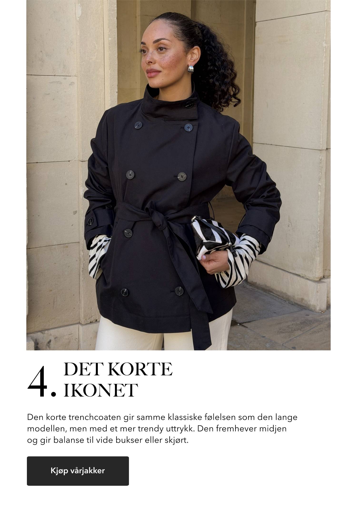 Kvinne iført en kort marineblå trenchcoat med knytebelte i livet, stylet med lyse bukser og mønstret clutch.