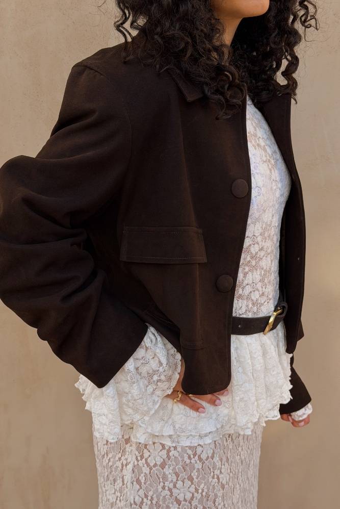 Kvinne i kort brun jakke over en hvit blondekjole.