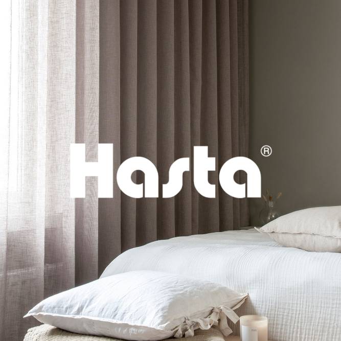 Hasta-verhot rauhallisessa makuuhuoneessa, jossa on valkoiset tyynyt ja pehmeät neutraalin sävyiset tekstiilit.