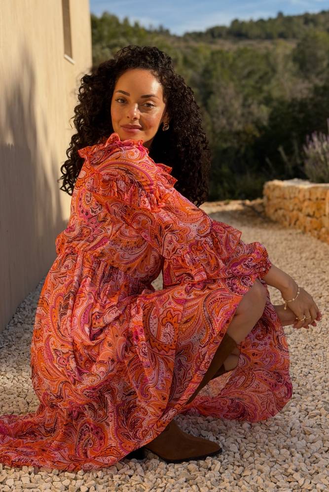 Kvinde i en flydende orange mønstret kjole udendørs i sollys.