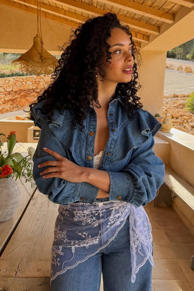 Kvinde i denimbluse med flæsedetaljer i en solrig udendørs setting.