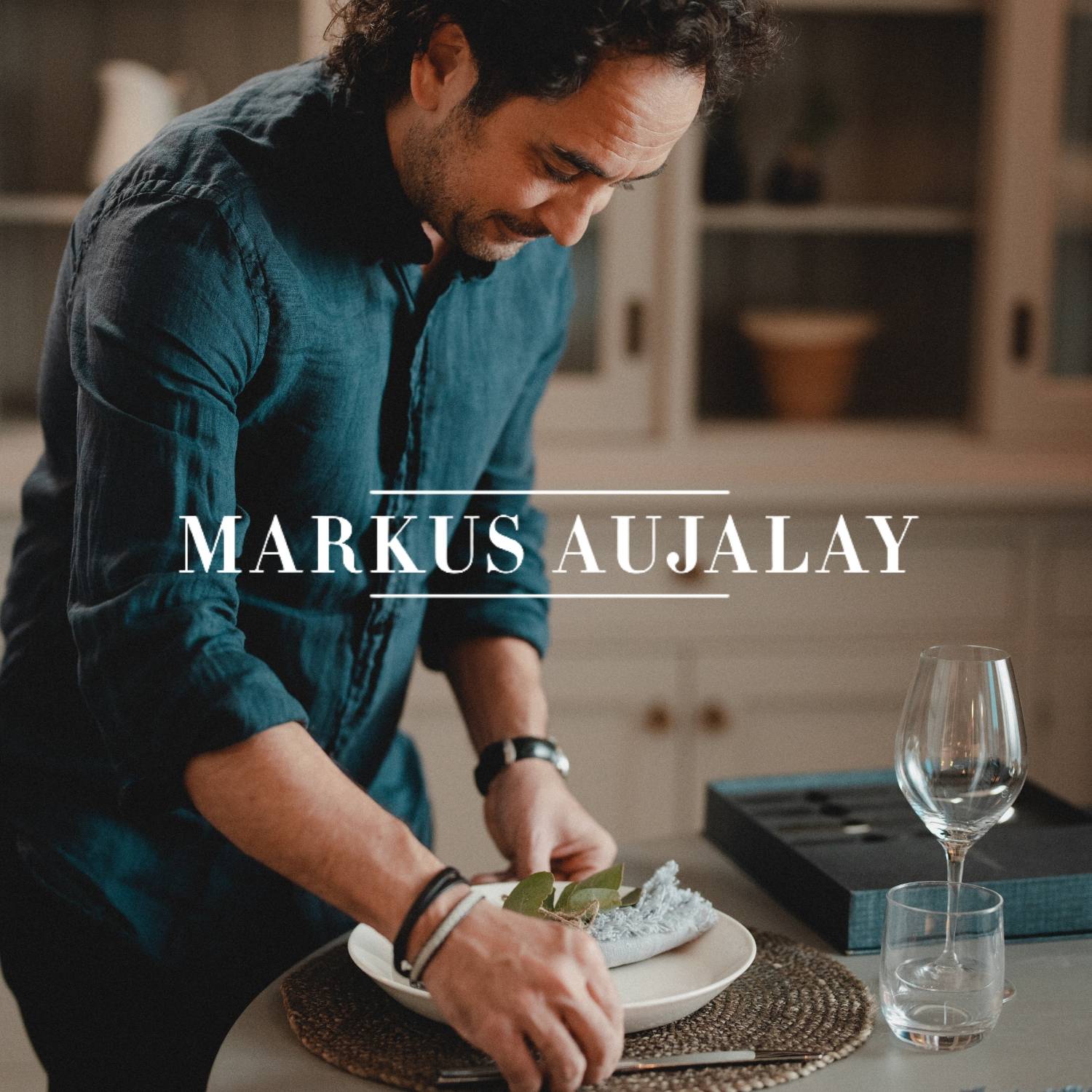 Mand dækker et bord i et køkken, med teksten “Markus Aujalay” vist på billedet.