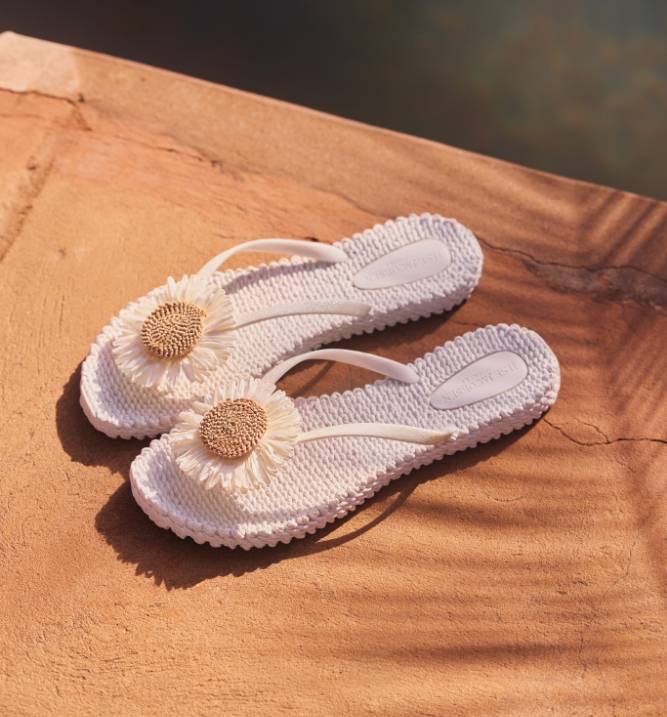 Et par hvide sandaler med blomsterdetaljer placeret på en solbelyst stenoverflade.