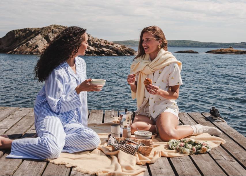 Kolme naista ulkona lämpimässä auringonvalossa yllään näyttäviä kuviollisia mekkoja ja juhlapukeutumista, mukana lähikuvia muotimuotokuvista sekä teksti ”The Dress Destination – Occasion Collection / SS26”.