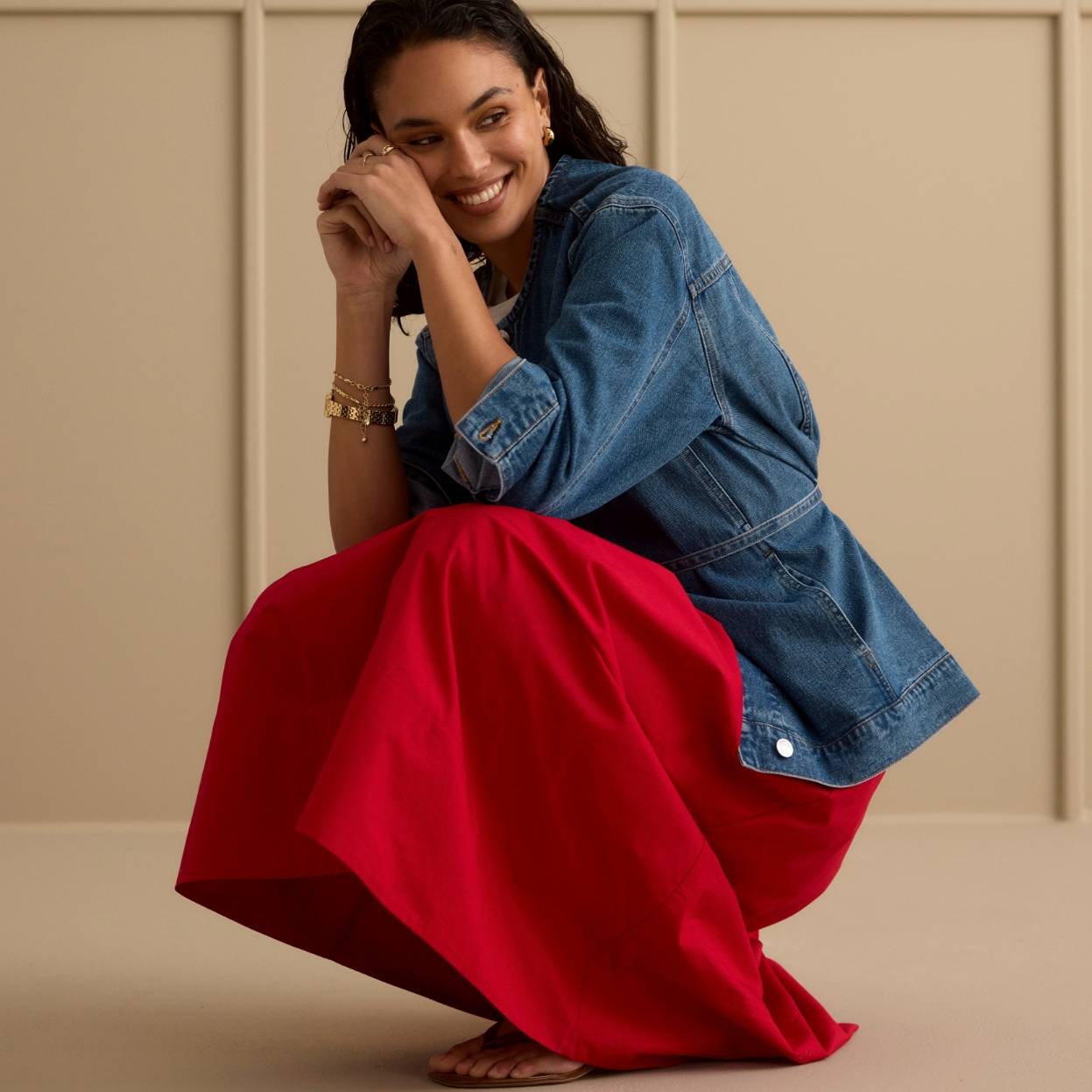 Kvinne i rød skjørt og denimskjorte i studiomiljø.