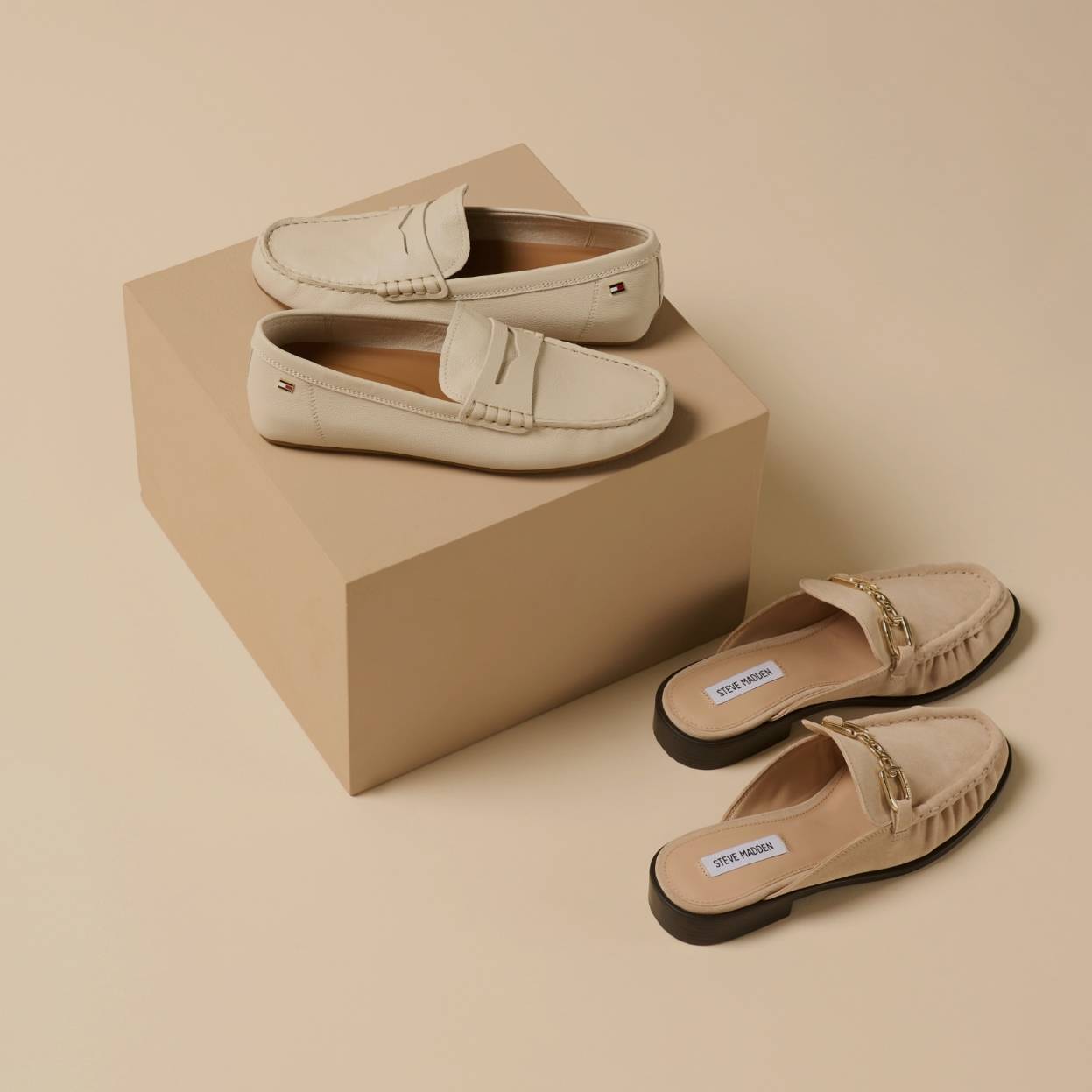 Loafers og sandaler i lys tone plassert på podie mot nøytral bakgrunn.